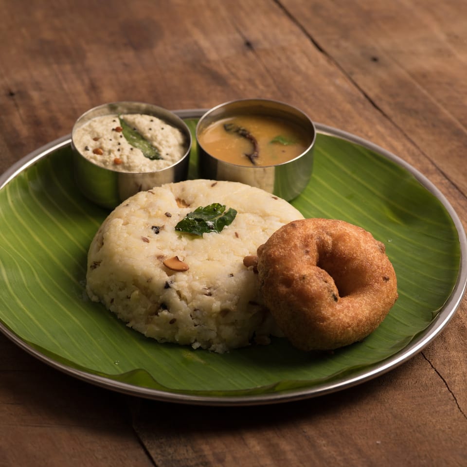 South Indian breakfast with upma, vada, coconut chutney, and sambar on a banana leaf.